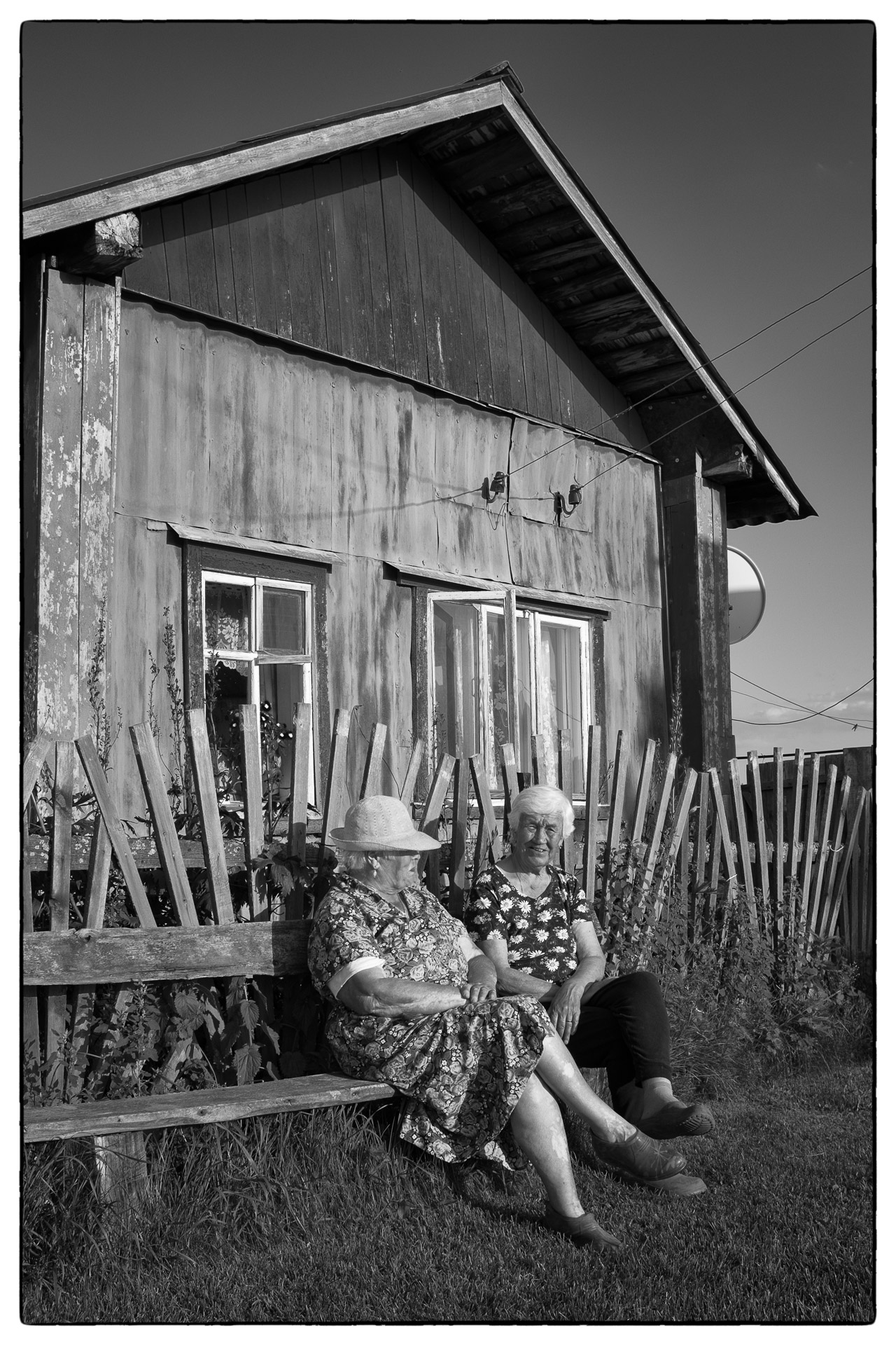 Due vecchiette sedute sulla panchina sullo sfondo di una casetta in legno